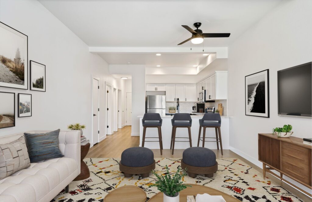 An open living room with a couch, bar stools, and a ceiling fan. The kitchen is visible in the background.
